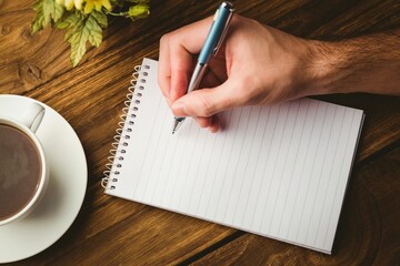 Cropped hand writing in book by coffee cup on table