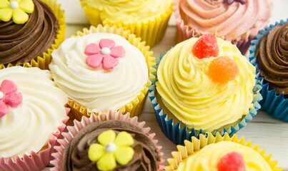 Flat design showing cupcakes on wood surface with liners, buttercream, fondant flowers, gumdrops
