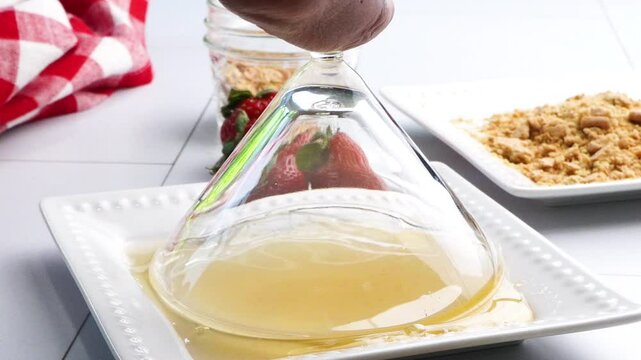 Dipping and rolling a martini cocktail glass into honey on a white plate. Making a cocktail and putting honey on the rim. Strawberry shortcake martini as a dessert drink with fresh berries.