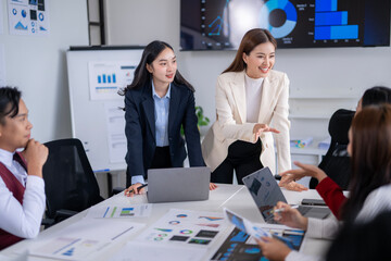 Asian businesswomen leading meeting with charts and laptops in office boardroom