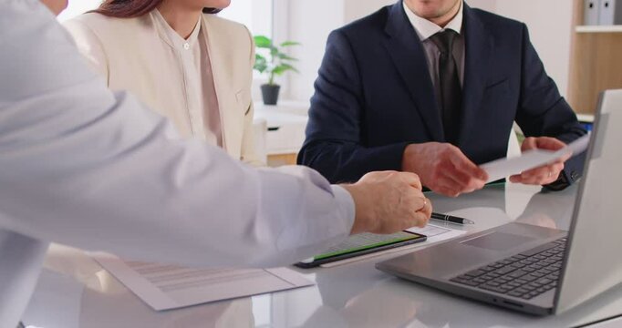 Team of business partners sitting at desk with modern technologies and papers, discussing project details, working on collaborative task, dressed in formal clothing, analyzing business strategies