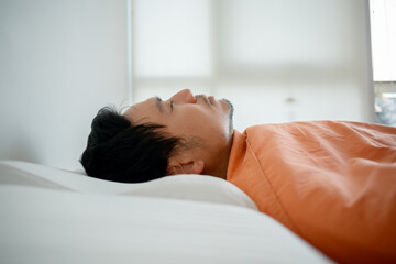 Asian man sleeping in bed with orange blanket