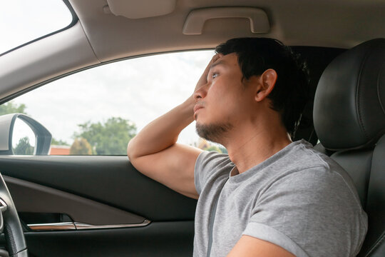 Asian man leaning head tiredly against car window