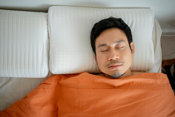 Asian man lying in bed with blanket and pillow