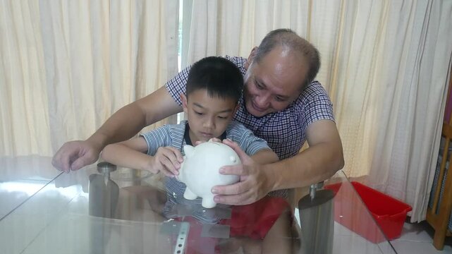 Father and son put coins into a piggy bank together.