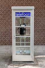 Vintage Dutch public telephone booth. A classic white booth against a brick wall.