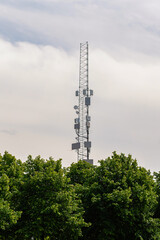 Modern telecommunications tower peeking out from the forest against the cloudy sky. Necessary...