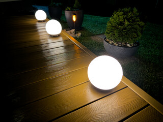 Evening garden lighting on WPC deck with glowing round lamps covered in rain droplets. Peaceful...