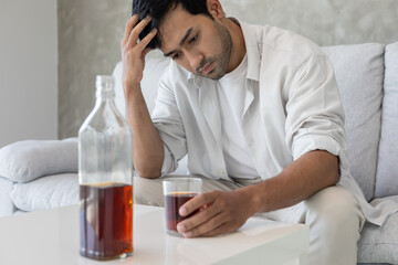 Depressed young man addicted feeling bad drinking whiskey alone at home, stressed frustrated lonely drinking alcohol suffers from problematic liquor, alcoholism, life and family problems