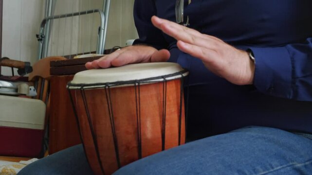 An artistic and rhythmic mood is captured as hands are poised over or actively playing the head of a djembe drum, highlighting the act of creating music