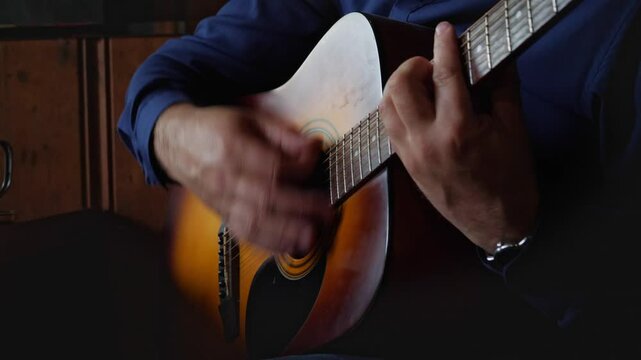 A creative and musical mood is captured by a close-up of hands expertly strumming the strings of an acoustic guitar, highlighting the intricate details of playing and the production of sound