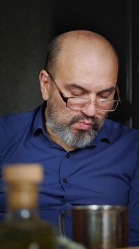 A contemplative and relaxed mood is captured as a bald man with a beard and glasses sips from a metal mug, looking down thoughtfully. This shot is ideal for depicting quiet moments of reflection