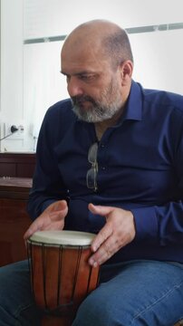 A focused and artistic mood is captured as a bald man with a beard intensely plays a djembe drum, his hands poised over the drumhead. This shot is ideal for depicting musical performance