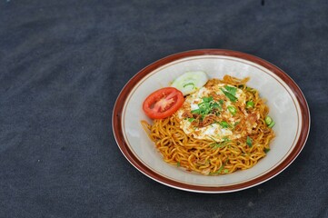 fried noodles with fried egg and sliced ​​cucumber and tomato on a white plate, on the table