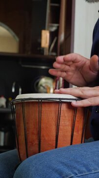 An engaged and artistic mood is captured as a bald man with a beard actively plays a djembe drum, looking up with an expressive and focused gaze. This shot is ideal for depicting musical performance