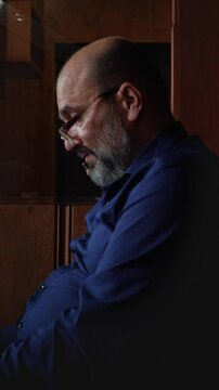 A focused and contemplative mood is captured as a bald man with a beard and glasses looks down intently, likely at a mobile phone or something held in his hands, suggesting deep concentration