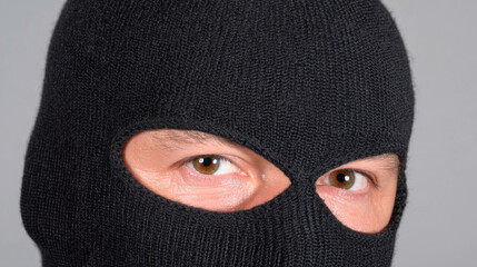 Person wearing black ski mask, with only their eyes visible, creates atmosphere of mystery and intrigue. intense gaze suggests hidden identity and evokes sense of suspense