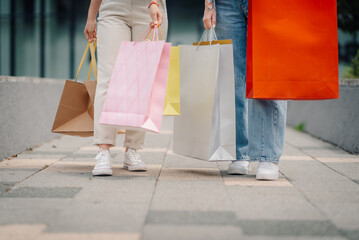Two happy customers walking and carrying shopping bags after purchasing in a city mall
