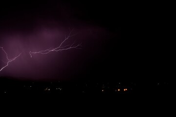 Lightning bolt striking the ground during a storm in Arizona. City lights are in the foreground.