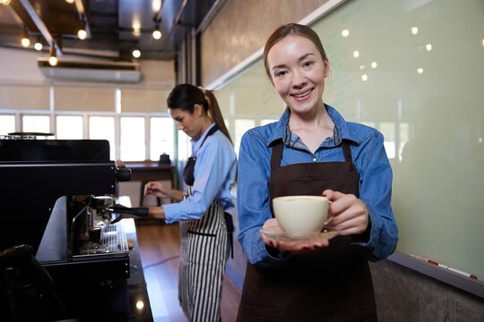portrait young barista woman holding a cup of coffee in the cafe