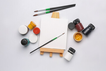 Mini easel with colorful gouache paints and brushes on white background