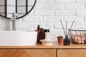 Sink bowl and bath accessories on wooden cabinet near white brick wall
