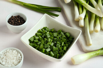 Board with fresh green onion and bowl of slices on white background