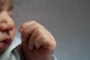 Newborn baby boy holding tiny fist near face