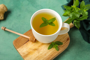Wooden board with cup of fresh mint tea and ginger root on grunge green background
