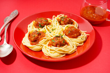 Plate of boiled pasta with tomato sauce and meat balls on red background