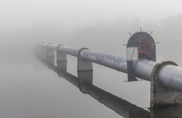 A minimalist image of a large pipe on a river disappearing into the fog.	