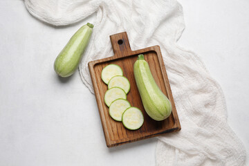 Wooden board with cut and whole zucchini on light background