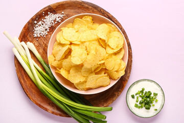 Bowl of tasty sour cream with sliced green onion and potato chips on lilac background