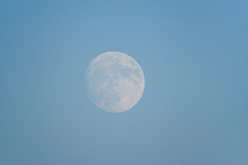 The full moon visible in broad daylight against a clear blue sky. © Schilo