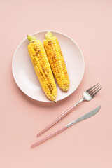Plate with tasty grilled corn cobs on pink background