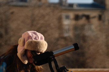 Girl in colorful jacket points while preparing solar telescope observation. Education, teaching, learning concept
