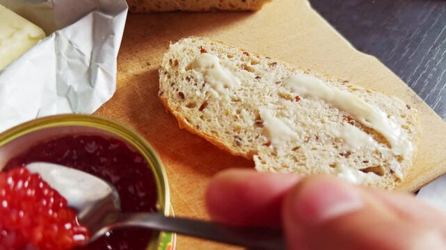 Fresh red salmon caviar being spread on buttered slice of bread