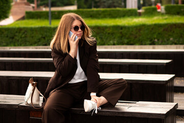 Young woman in brown suit sitting on wooden benches outdoors. Great natural vibe and showcase stylish, relaxed mood. Outfit looks effortlessly chic