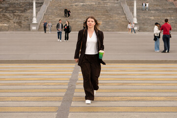 Young woman walking confidently on crosswalk, holding a coffee cup outdoors.