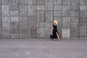 Woman in black polka-dot dress posing against concrete wall.