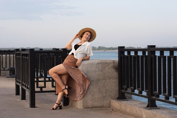 Smiling woman reclines on river wall in summer outfit
