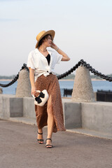 Woman walks stylishly holding handbag at sunset along promenade.