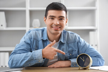 Young man pointing at alarm clock in office