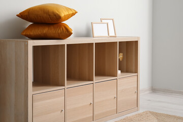 Wooden cabinet with cushions and blank frames near white wall