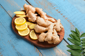 Board with fresh ginger roots and slices of lemon on blue wooden background