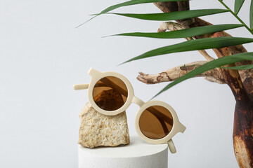 Decorative podium with stylish sunglasses and palm leaf on white background