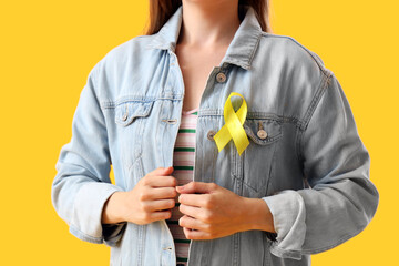 Woman with yellow awareness ribbon on color background, closeup