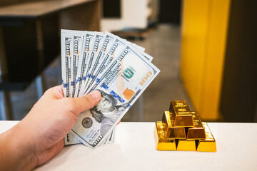 Gold and dollar bills are placed together on a table, reflecting the idea of ​​the need to produce a denominated dollar with a gold base value.