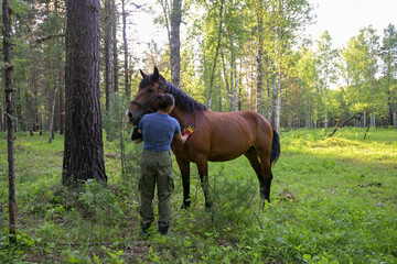 rustic man with  horse in rural village near  forest.  horse farm is surrounded by nature, hay is stacked nearby,  peaceful and traditional.  man is caring for  horse