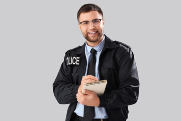 Male police officer with notebook on grey background